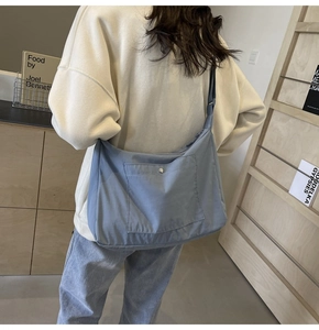 Blue nylon crossbody bag with front snap pocket shown on model in a cozy library setting