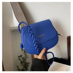 Detail of bright blue crossbody bag with braided shoulder strap and gold text logo