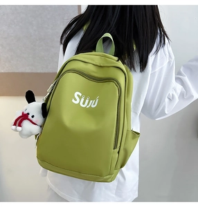 Close-up of avocado green nylon backpack featuring white Suju logo and a plush dog charm