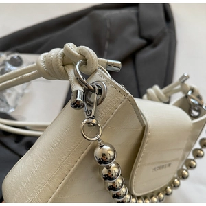 Detail of cream shoulder bag featuring silver bead chain and elegant knotted leather strap