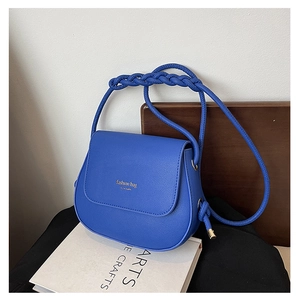 Close-up of royal blue crossbody bag with braided strap on an arts book background