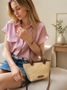 Detailed close-up of straw woven tote bag featuring brown leather knot handle and logo
