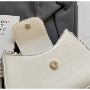 Detailed macro view of cream-white bag featuring ribbed texture and pearl chain strap