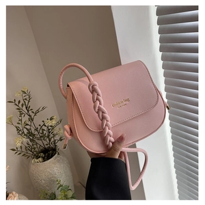 Close-up of pink crossbody saddle bag with braided strap and gold fashion lettering