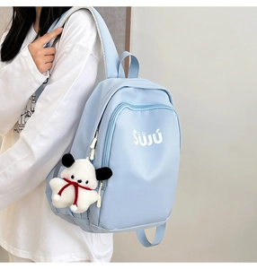 Detail view of light blue nylon backpack with SUJU logo and white puppy plush keychain