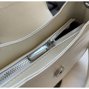 Macro detail of silver zipper and magnetic buckle on white croc-embossed handbag