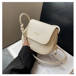 Macro shot of a cream-colored crossbody bag with braided handle and textured leather finish