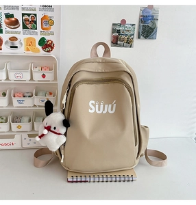 Detail of beige nylon backpack with SÜJÚ print, cute dog pendant and student stationery