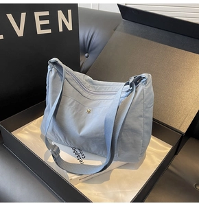 Close-up of light blue nylon bag with metal snap button pocket and adjustable strap