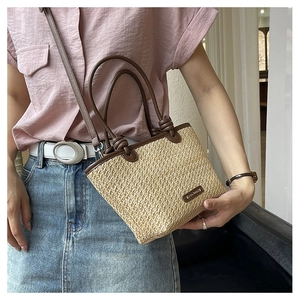 Detail of woven straw handbag with brown leather knot handles and adjustable strap