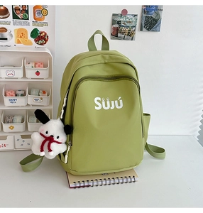 Close-up of grass green canvas backpack featuring white SÜJÚ logo and plush doll pendant