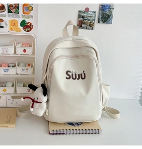 Detail of canvas backpack with SÜJÚ logo and plush puppy charm on a side zipper