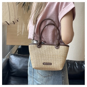 Detail of a straw woven bucket bag with brown leather handles and knot decoration