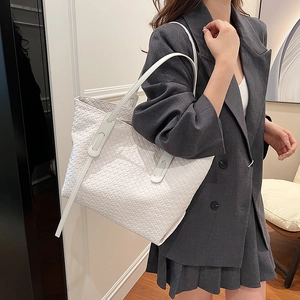 Large white woven tote bag shown at a 45-degree angle on a fashion model in a grey suit