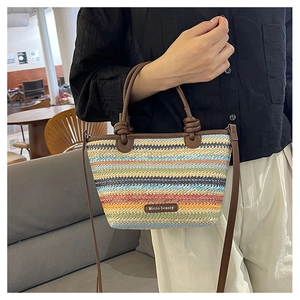 Detail of colorful striped straw woven bag with brown leather knotted handles and logo tag