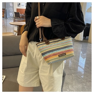 Detail of colorful striped woven straw bag with leather handles and metallic brand plaque