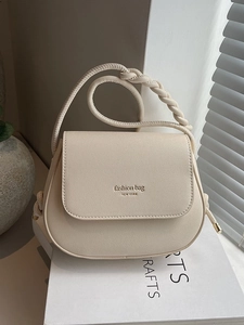 Minimalist beige saddle bag with woven rope strap and gold lettering on white prop