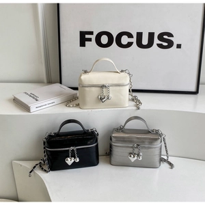 Détail de trois mini sacs seaux en cuir crème, noir et argent avec bandoulières en chaîne