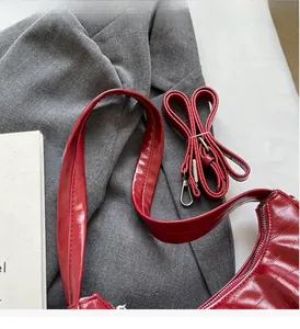 Détail du sac croissant en cuir verni rouge brillant avec deux bandoulières sur tissu