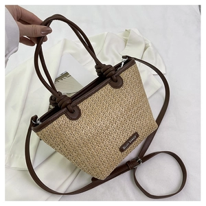 Detail of straw woven bucket bag with brown leather handles and metal brand plate
