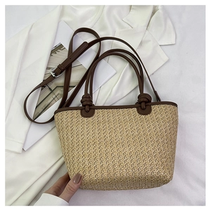 Close-up of woven straw tote bag with brown leather handles and decorative knots