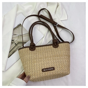 Detail of hand-woven straw tote bag with brown leather handles and brand logo tag