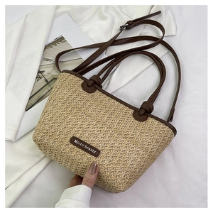 Detail of woven straw tote bag with brown leather handles and adjustable shoulder strap