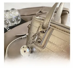 Détail macro du charm sphérique métallique sur un sac seau champagne à motif crocodile