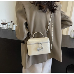 Détail du sac vanity crème gaufré crocodile avec breloque cœur et bandoulière sur mannequin