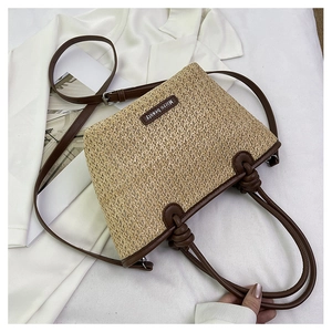 Detail of straw tote bag with brown leather handles and Micro beauty logo on white blazer