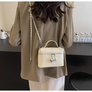 Détail d'un mini sac boîte beige en cuir avec breloque cœur et bandoulière chaîne