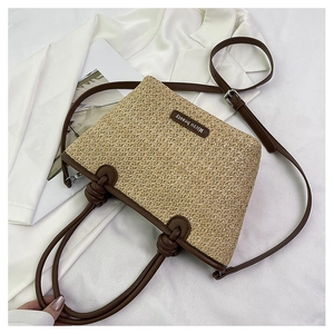 Close-up of woven straw bag with knot handles, brown trim, and adjustable crossbody strap