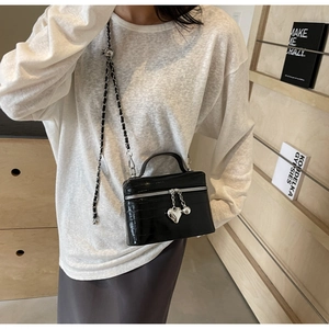 Détail du sac bandoulière noir motif crocodile avec chaîne argentée et breloque cœur