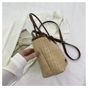 Close-up of the woven straw bucket bag with dark brown leather straps and detail