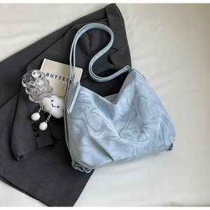 Détail du sac cabas bleu clair à texture fluide avec écusson logo sur un blazer gris