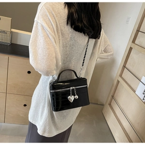 Détail du sac bandoulière en cuir verni noir avec pendentif cœur et zips argentés