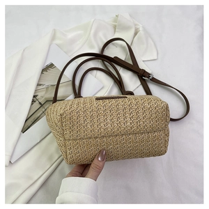 Detail of woven straw handbag with brown leather handles on white silk and magazine