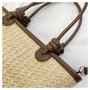 Detailed view of woven straw tote bag featuring brown leather knot handles and silver metal hooks