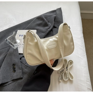 Détail du sac croissant crème montrant la texture cuir plissée et la plaque logo en métal