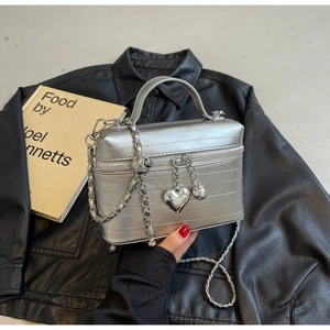 Détail macro d'un sac boîte en cuir argenté brillant avec breloques cœur et chaîne