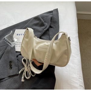 Détail du sac beige avec motif crocodile et plaque logo argentée sur le devant du sac