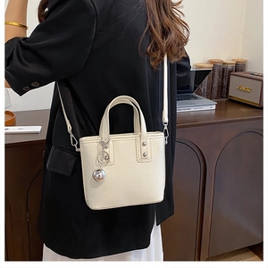 Gros plan sur le mini sac seau crème avec rivets argentés et pendentif boule métallique