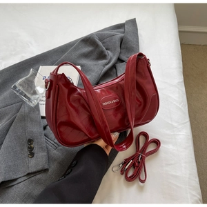 Détail d'un sac demi-lune en cuir verni rouge foncé avec bandoulière réglable