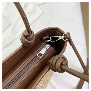 Detail of woven straw tote bag featuring brown leather trim and knotted handle detail
