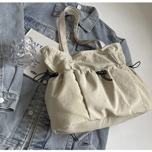 Detailweergave van beige draagtas met geplooide textuur en trekkoordzakken op denim jasje