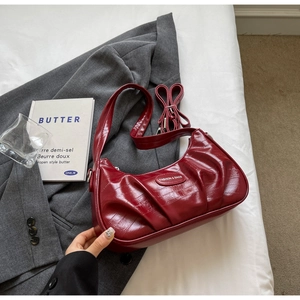 Détail macro du sac croissant plissé bordeaux en cuir brillant avec plaque logo en métal