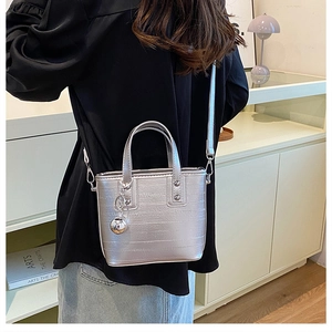 Détail d'un sac seau argenté à texture métallique avec accessoire pendentif en forme de bille