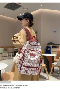 Detail eines weißen Graffiti-Rucksacks mit weinroten Trägern und Plüschbär-Anhänger