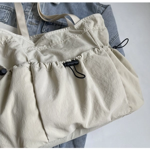 Detail van beige geplooide draagtas met multi-pocket design en trekkoord gespen