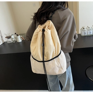 Rear view of model wearing a cream nylon backpack with drawstring closure and mesh bottom